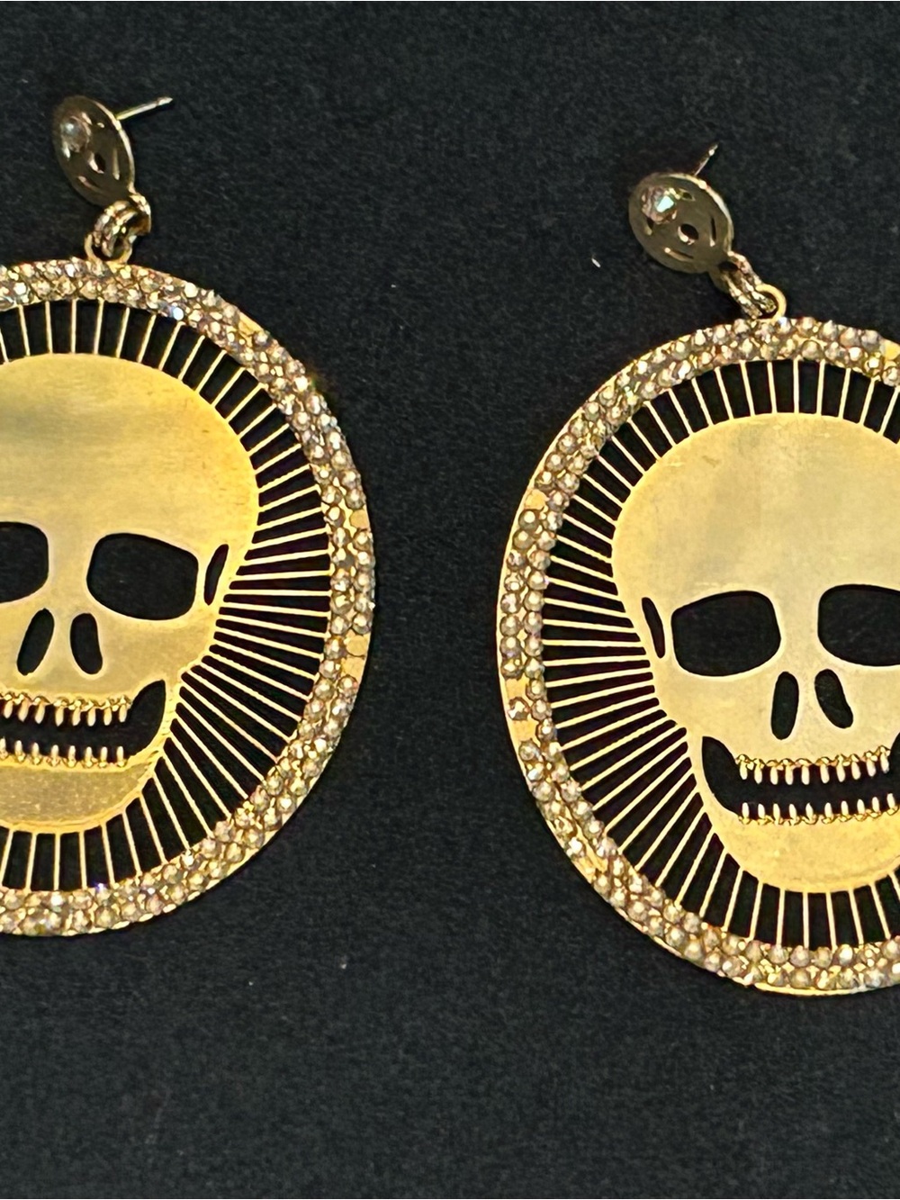 Gold tone dangling earrings featuring a cutout skull design in Crystal pave fram